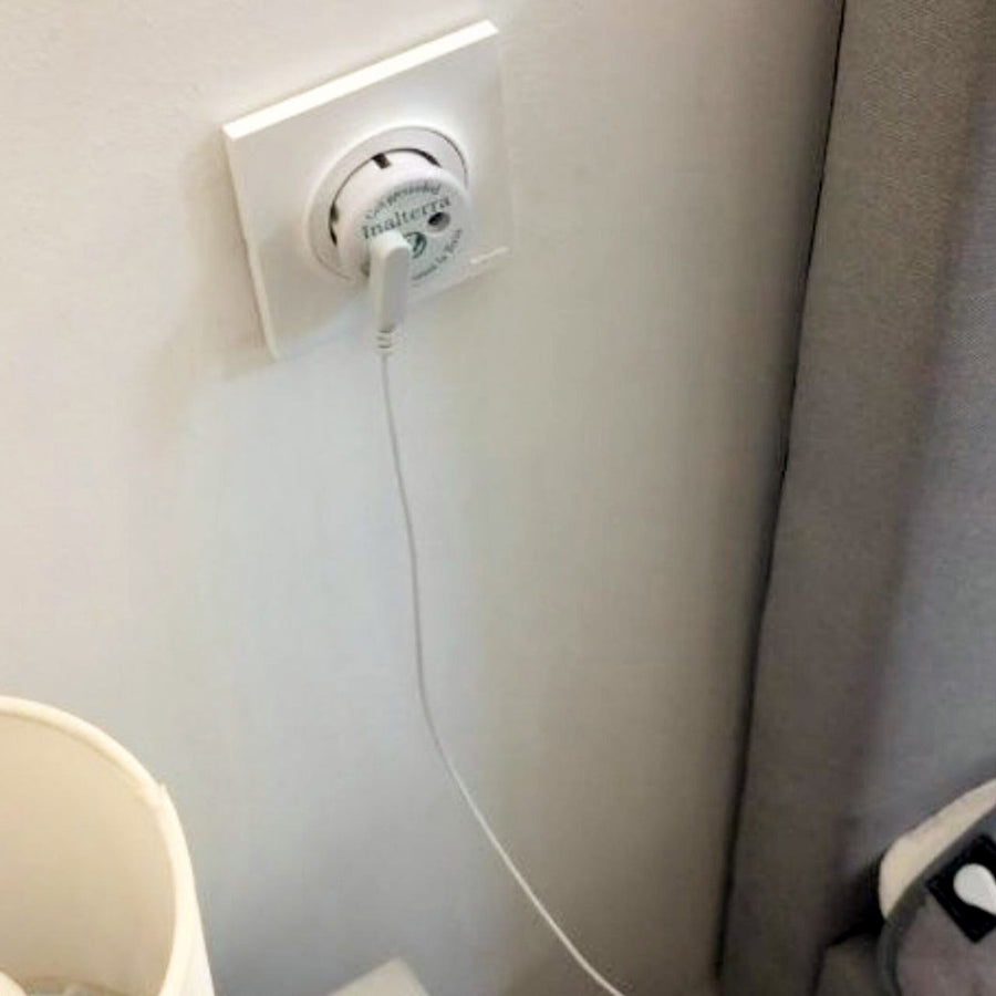 Adaptateur de prise terre Inalterra branché au mur, câble blanc relié au surmatelas du lit