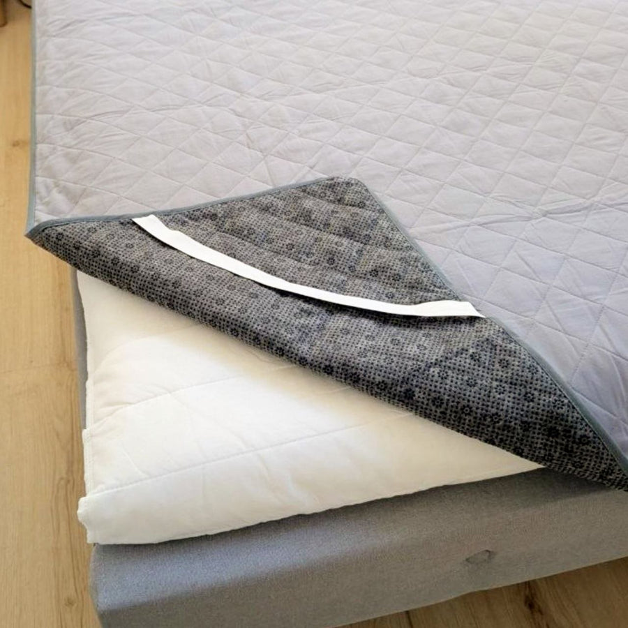 Coin du surmatelas de mise à la terre Inalterra relevé, montrant la sangle élastique et le dessous antidérapant