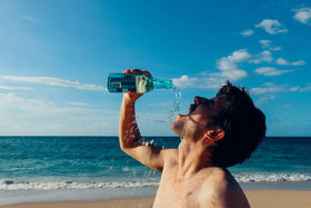 homme sur la plage qui boit de l'eau de bouteille en verre